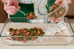 chopped tomatoes and herbs are placed on top of the cod fillet with a spoon in a baking dish